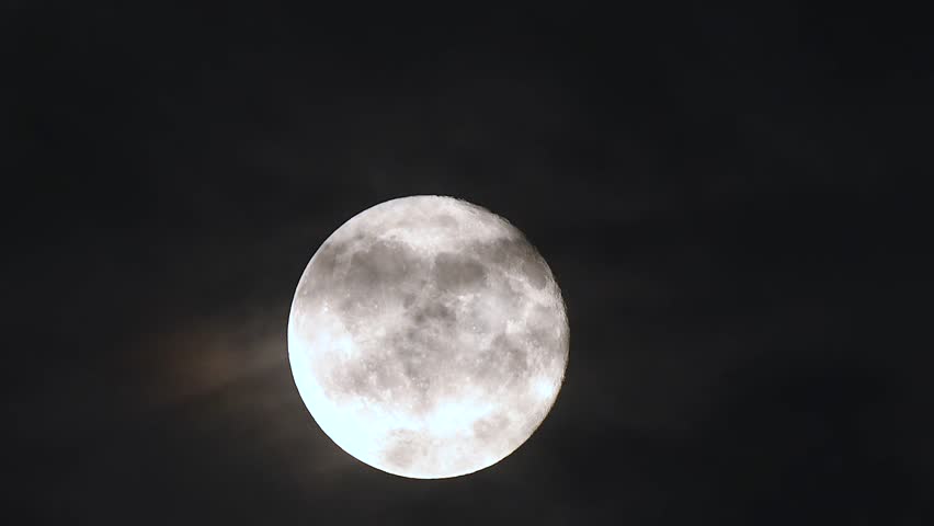 Cinematic time lapse of full moon rising through clouds on a dark sky during twilight