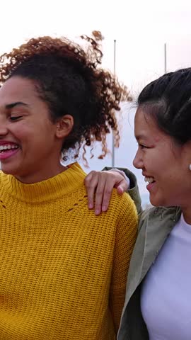 Vertical HD video of happy young group of multiracial women hanging out at city street. Diversity, youth community and female friendship concept with multiethnic girls talking and having fun outside