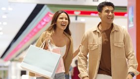 Happy Asian family man and woman shopping, buying goods at department store. Couple enjoy urban lifestyle holding shopping bag walking and looking at store in shopping mall on summer holiday vacation. - Powered by Shutterstock - Get 15% off with code: PIKWIZARD15