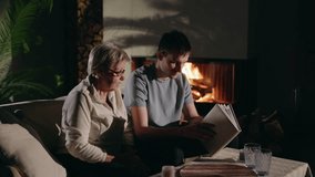 A grandmother and her grandson share a quiet moment by the fireplace, flipping through a photo album and cherishing family memories in a warm setting. High quality 4k footage - Powered by Shutterstock - Get 15% off with code: PIKWIZARD15