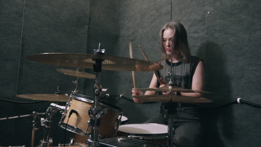 Woman drummer practicing in music rehearsal studio wearing black outfit, playing wooden drum kit with intense focus, modern musician vibe