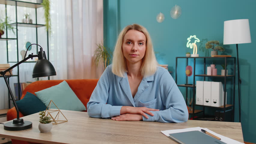 Young businesswoman smiling friendly at camera and waving hands gesturing hello, hi, greeting or goodbye, welcoming with hospitable expression at home office workplace desk. Happy girl in living room.