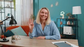 Young businesswoman smiling friendly at camera and waving hands gesturing hello, hi, greeting or goodbye, welcoming with hospitable expression at home office workplace desk. Happy girl in living room. - Powered by Shutterstock - Get 15% off with code: PIKWIZARD15