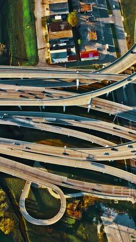 Aerial perspective of Dallas showcasing a complex network of highways and roads intertwining amidst urban development, with greenery visible nearby and vehicles in motion.