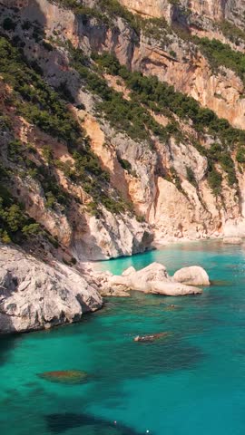 Aerial drone view on white sand Cala Goloritze in Orosei Gulf of Sardegna, Costa Smeralda. Warm turquoise sea, small beach and boats with green mountains on the Sardinia island.
