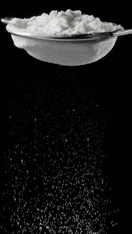 Sift icing sugar or powdered sugar through a sieve tool on black background.