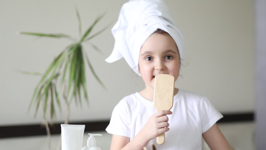 Cute little girl having fun at home in the bathroom. Kid holding hairbrush like a microphone and singing