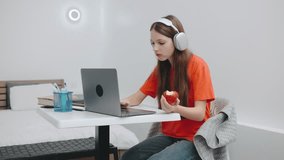 A teenage girl studying at a desk with headphones while eating an apple in a modern room with minimalistic decor - Powered by Shutterstock - Get 15% off with code: PIKWIZARD15
