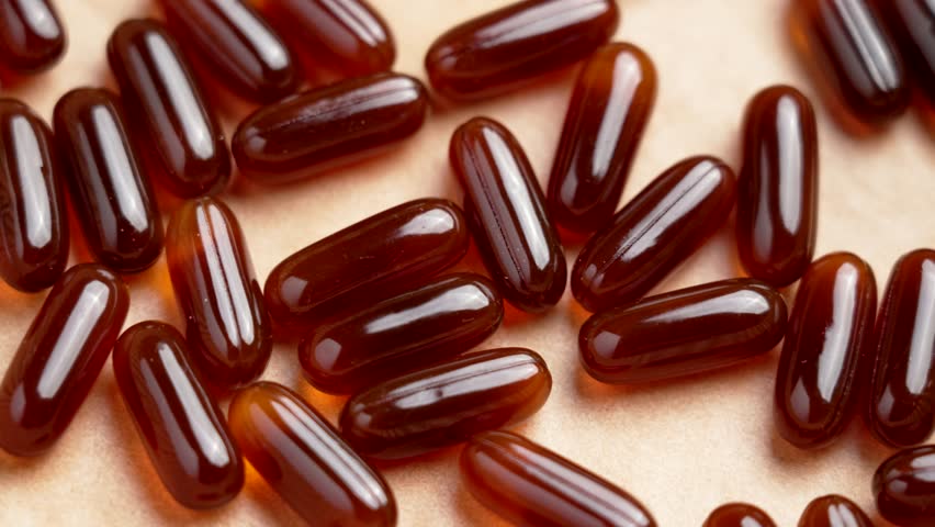 Gel vitamin capsules on brown paper sheet. Translucent tablets of dietary supplements. Top view. Rotation