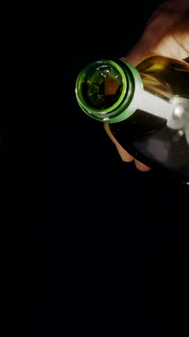 Extra virgin olive oil is being poured out from an olive oil bottle on black background. Slow motion vertical template.