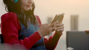 Young smiling asian woman in red sweater and wireless headphones resting with smartphone, enjoying music playlist for Relax and enjoying a peaceful moment outdoors at sunset. - Powered by Shutterstock - Get 15% off with code: PIKWIZARD15