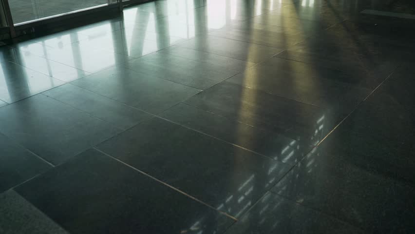 Sunlight creates reflections on a polished granite floor near glass doors in a modern building