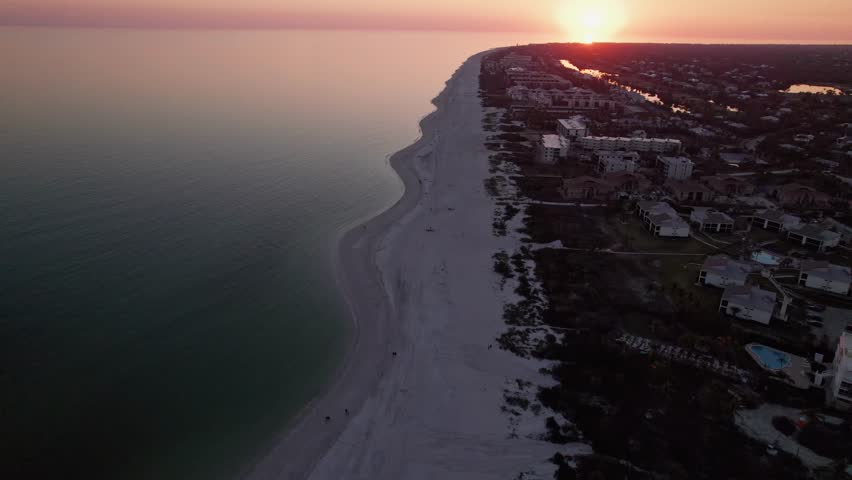 Drone view of Sanibel Island, FL beachfront at sundown as beach vacationers walk along Ocean and Gulf of Mexica sand and sea waves under warm sun rays at tropical island resort and travel landscape