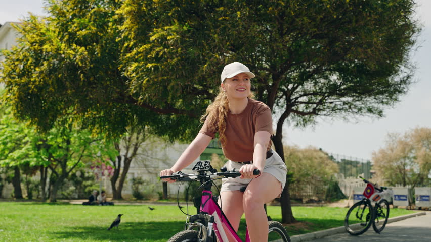Woman rides rental bike on Buyukada Island, explores urban scenery. Female cyclist enjoys leisure ride, historic architecture, rich green surroundings. Casual biking trip, eco-friendly travel.