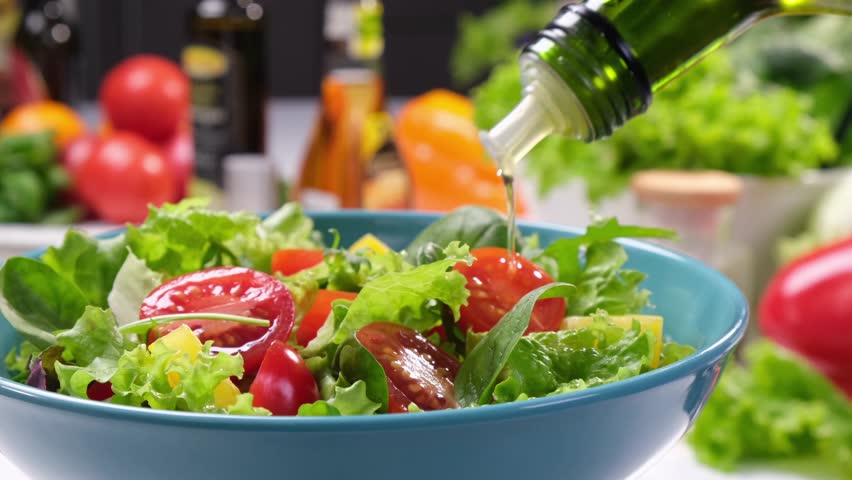 Salad being drizzled with olive oil from a bottle, fresh leaves and tomatoes on modern kitchen background close-up