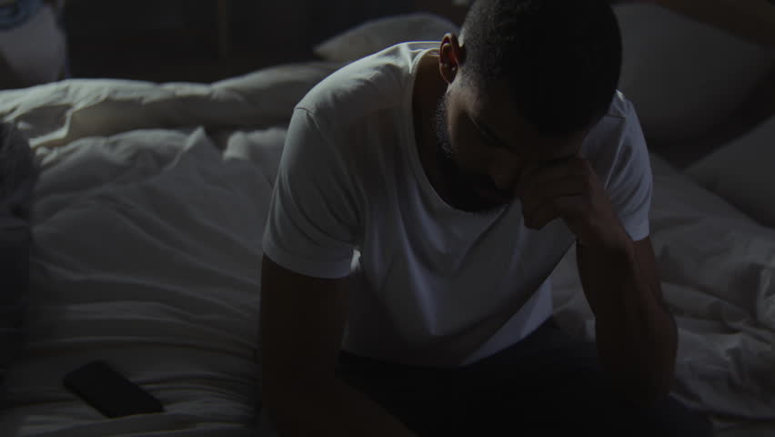 Sad black man ignores calls trying to survive difficult breakup in bedroom. African American guy hides from friends dealing with mental illness alone