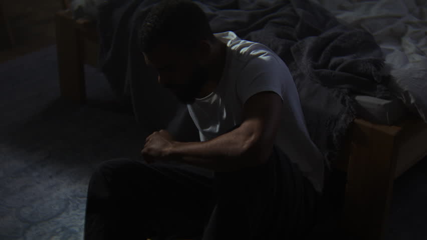 Pensive African American guy calms down with self hugging sitting on room floor. Black man with depression disorder survives mental illness attack alone
