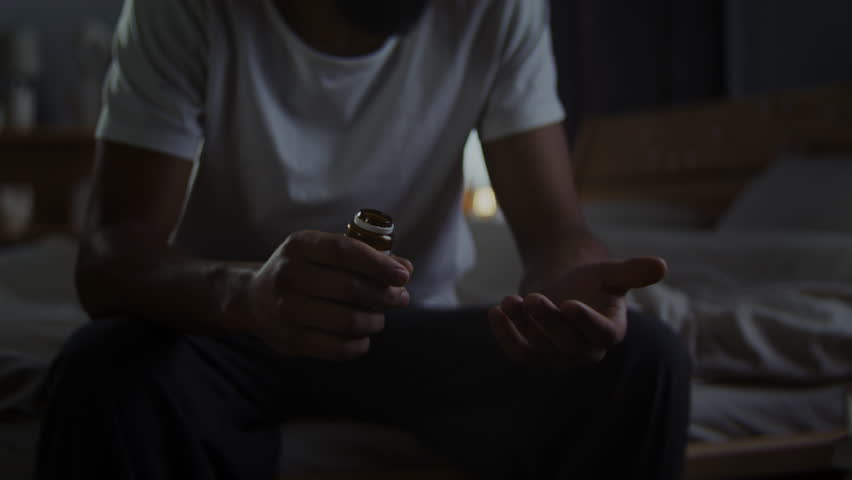 African American man takes pills and drops bottle during panic attack at home. Black male survives depression disorder with pharmaceutical therapy