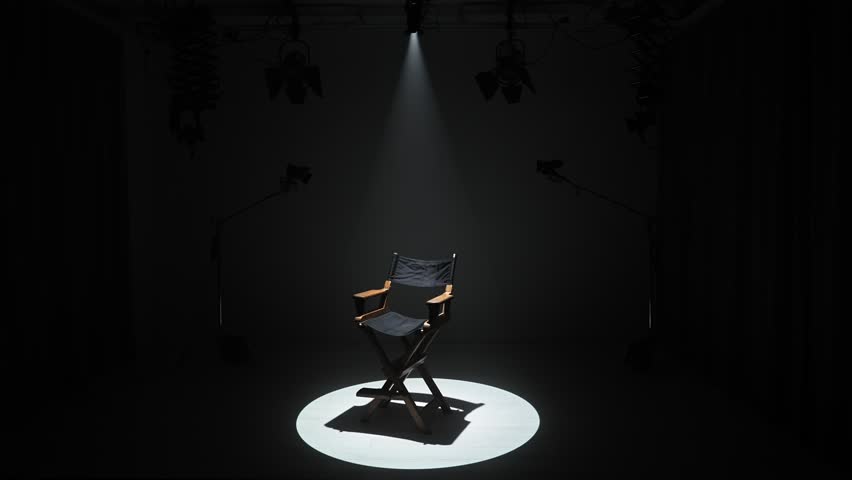 Studio for photo video production filming with lighting equipment and cyclorama, team member prepares lights and camera, director chair in the middle under spotlight