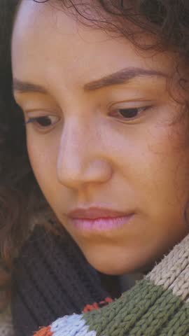 Vertical: An extreme close-up of a young Latina woman's face, highlighting her sad, desolate expression. Her eyes are vacant as she stares into the void, lost in her overwhelming emotions.