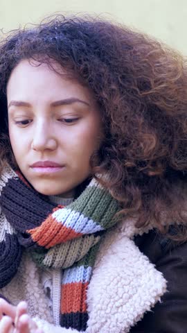 Vertical: young Latina woman with curly hair, wearing a white sweater and colorful scarf. Her eyes are filled with tears, her expression heart-wrenching as she tries to hold back her sadness.
