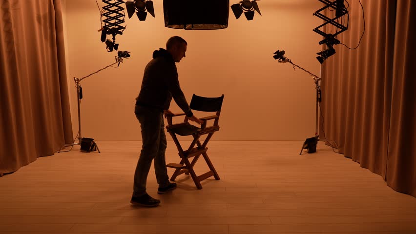 Studio for photo-video shooting with lighting equipment. Team members set up the lights, set up the camera and bring in the director's chair.