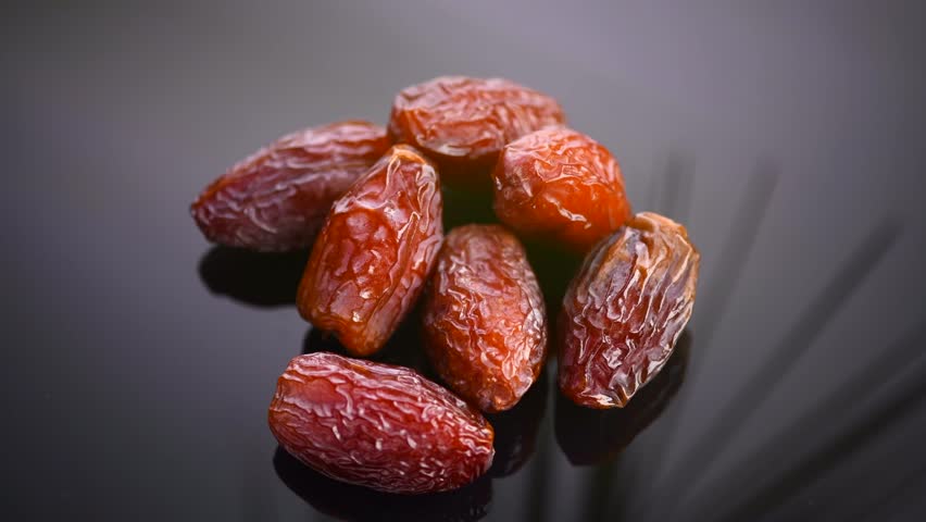 Dates fruit. Date fruits with palm tree leaf reflection on black background. Heap of Medjool dates close up. 