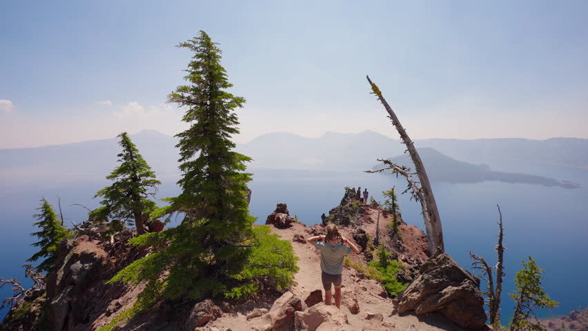 A young girl walks toward a breathtaking mountain overlook, gazing at the spectacular deep blue waters of Crater Lake below.