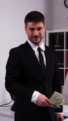 Young attractive businessman joyfully throwing his money dollars hundred banknotes in slow motion. Modern office with armchair and desktop. Steadicam. Vertical Shot.