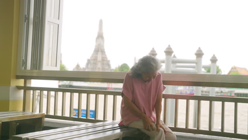 Travel and health insurance concept. Asian elderly woman get injury knee pain or leg cramp during travel in the city. Senior woman tourist travel Buddhist temple in Thailand on summer holiday vacation