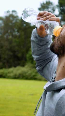 Portrait of fitness man drinking water from bottle splashing water in face cooling down after running workout in park. Refreshment drink sweating after intense exercise. Slow motion close-up back view