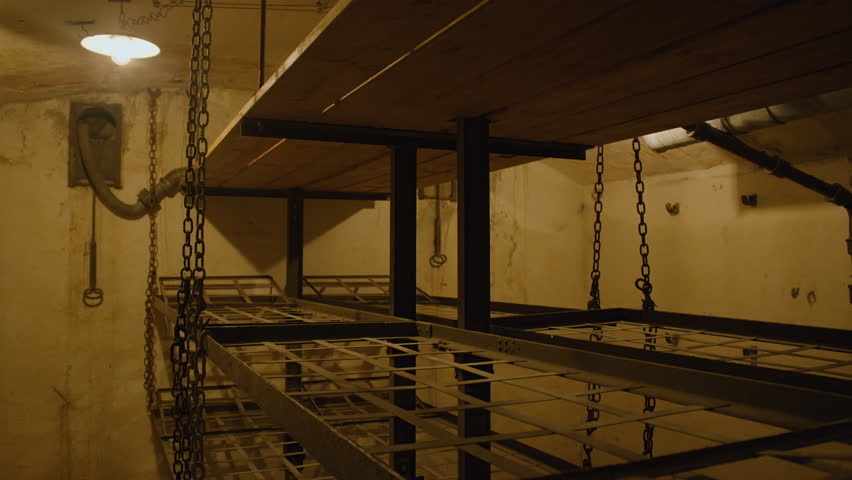 A dimly lit bunk room with bunk beds suspended by chains. Bunk room in Fort de Mutzig fortress.