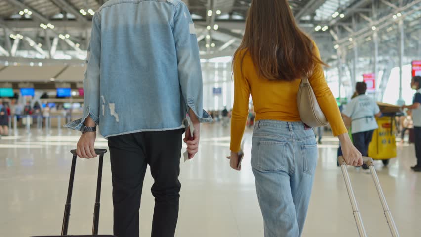 Rear view of young couple walking in airport terminal to boarding gate. Attractive man and woman friends passengers feel happy and excited for going travel abroad by airplane for holiday vacation trip