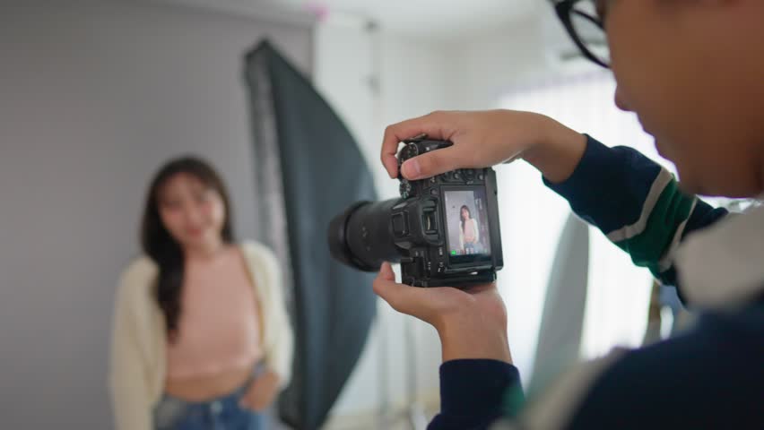 Asian cameraman shooting woman model with backdrop in photography studio. Attractive professional photographer taking beautiful pictures using techniques to create images for advertisement or movies.