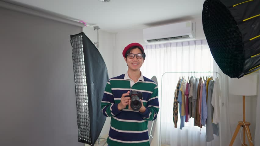Portrait of Asian cameraman shooting model in the photography studio. Attractive professional photographer taking picture using filming techniques to create image for advertisement and look at camera.