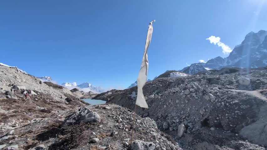 A white prayer flag flutters in the strong wind atop a flagpole planted in the vast Ngozumba Glacier, a symbol of spirituality and resilience amidst the harsh beauty of the Himalayas