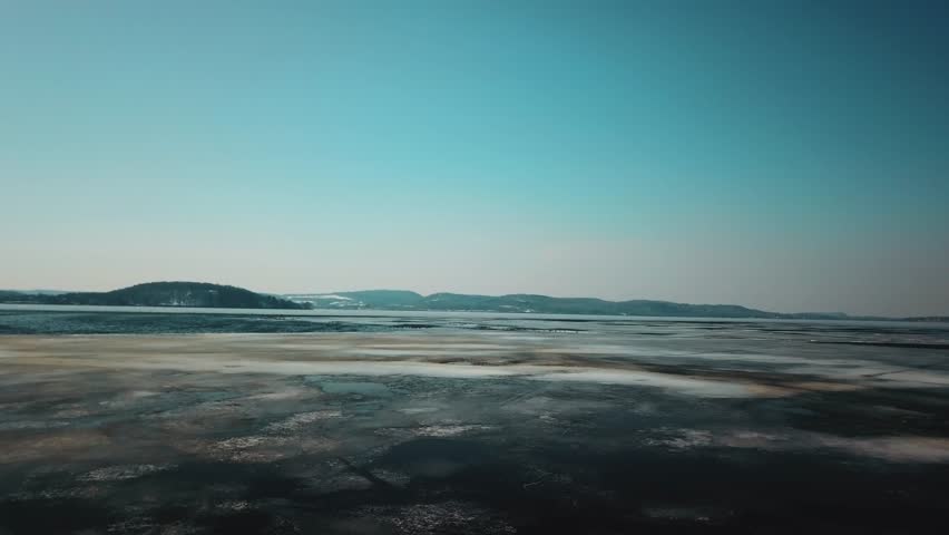 A wide aerial view of a frozen lake in Wisconsin during winter, showcasing ice patterns and distant hills under a clear sky.