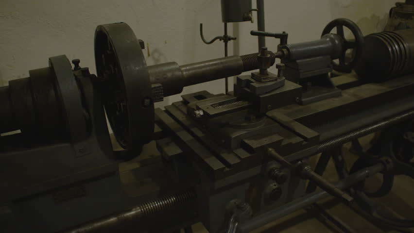An old, industrial-style lathe machine with a variety of gears, levers, and wheels sits against a wall, illuminated with dim light. Industrial elements in the interior of Fort de Mutzig fortress
