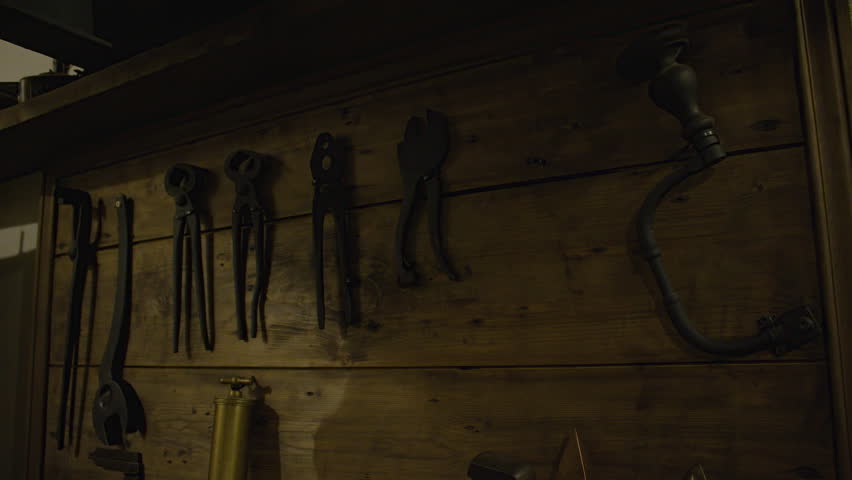 A close-up shot of a dark wooden wall and various old tools hanging on it, such as pliers, screwdrivers, a wrench. Interior of Fort de Mutzig fortress, now a museum.
