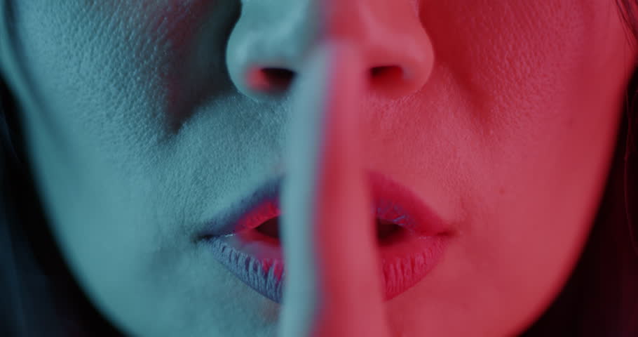 Close-up of woman touching lips with finger asking to be quiet in neon light. Hand gesture and people concept.