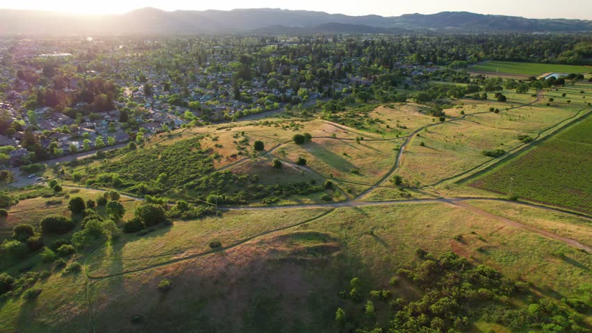 Napa Valley, California. Slow aerial wide pull-in revealing lush, vibrant green rolling hills along a hiking trail as the sun rises behind the valley
