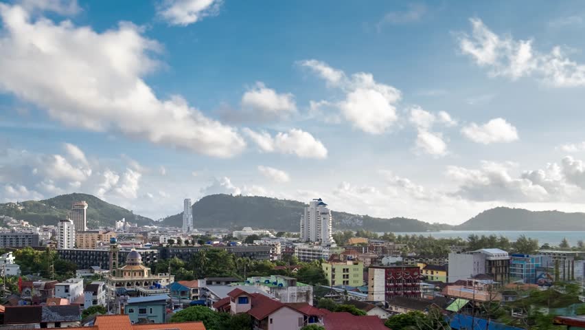 Dynamic timelapse over Patong, Phuket: Vibrant cityscape nestled between lush mountains and azure sea. Dramatic rainy clouds roll across the sky, casting ever-changing shadows on the bustling Thailand