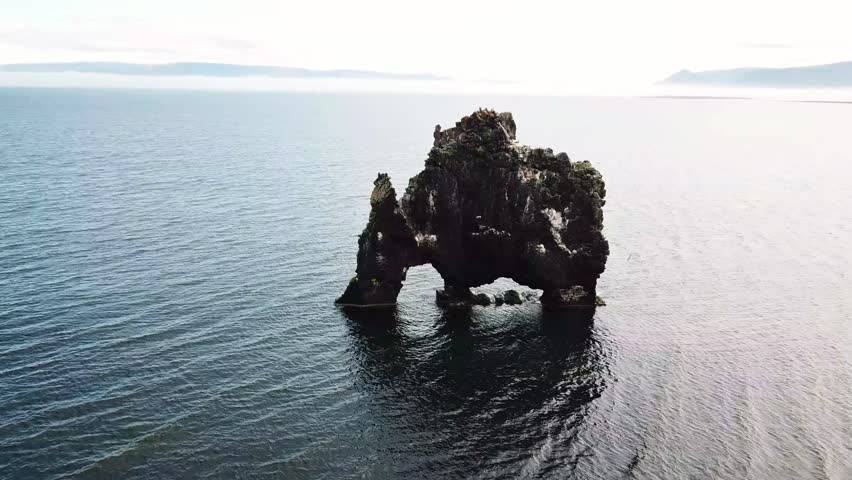 Stunning view of Hvítserkur, a majestic rock formation in Iceland, standing tall in the ocean with its unique arch-like structure, surrounded by serene, rippling waters and mountainous landscapes