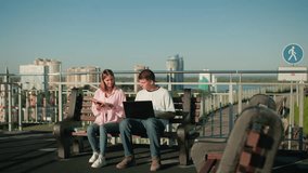 Male and female students studying outdoors on a bench; male typing on laptop while engaging with female partner reading from her book, set against an urban skyline backdrop - Powered by Shutterstock - Get 15% off with code: PIKWIZARD15