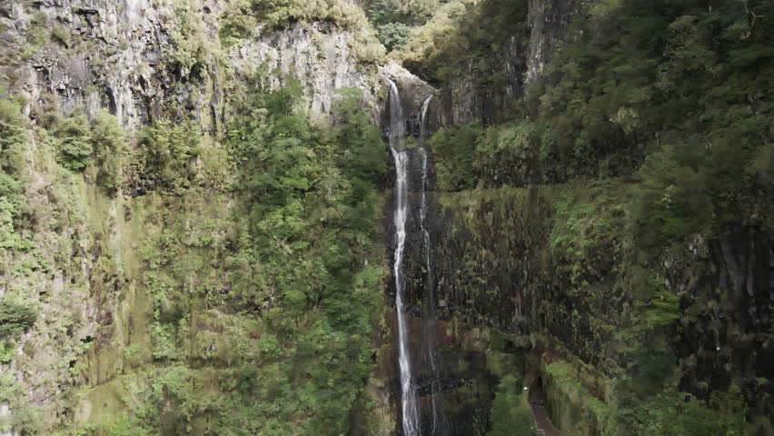 A stunning drone shot approaching the Garganta Funda waterfall in Madeira Island. Captures the towering cascade, rugged cliffs, and lush surroundings. P