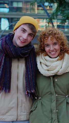 Vertical video of young happy group of diverse friends in warm clothes smiling at camera standing together outside. Portrait of millennial people enjoying winter vacation. Friendship concept
