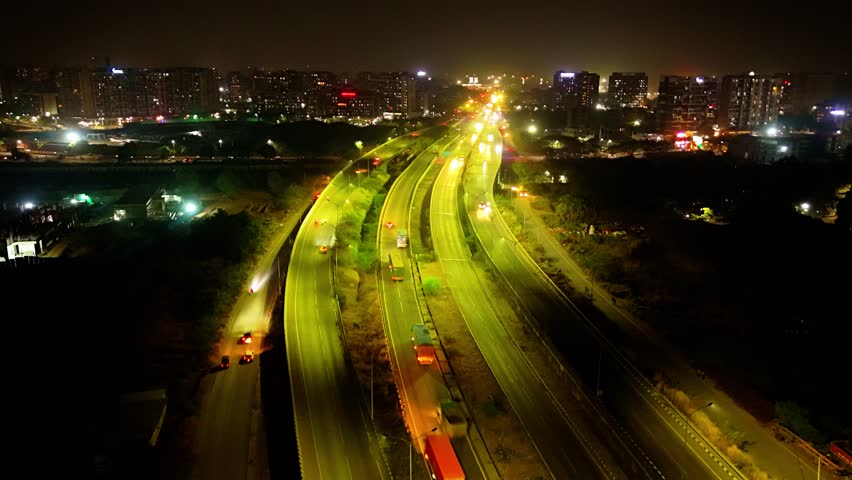 Aerial view time lapse of Lit Up expressway with traffic, Illuminate overpass at night along moving vehicle, Bright highway bridge, Car passing Beneath, Colorful lights under motorways, Hyperlapse