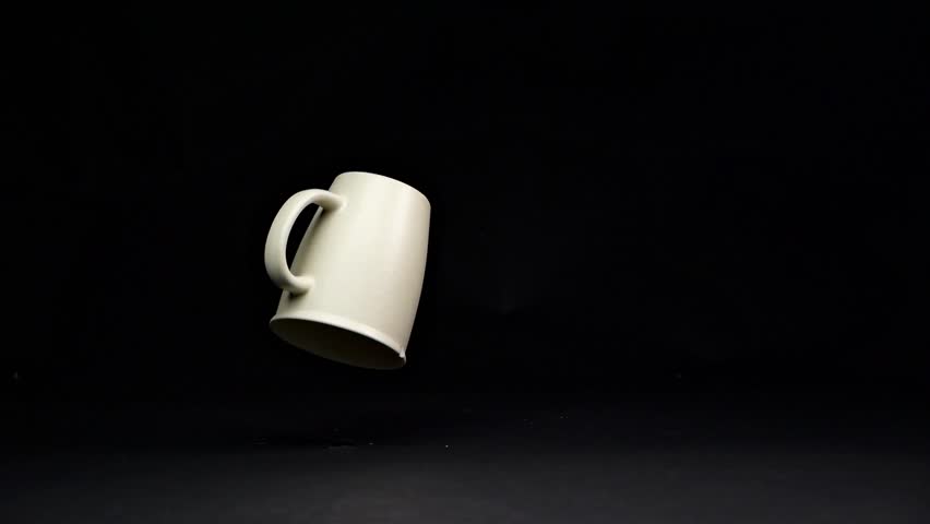A bright mug falls and shatters on the floor in slow motion, with fragments scattering in all directions against a matte black background.