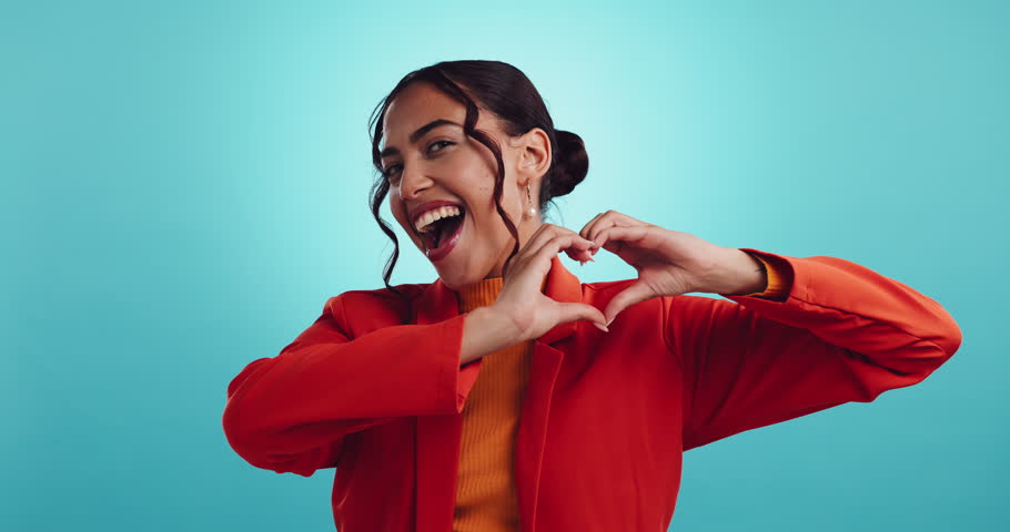 Heart, hands and face of woman in studio with gesture for love, gratitude and thank you on blue background. Emoji, symbol and portrait of person with sign for romance, valentines day and kindness