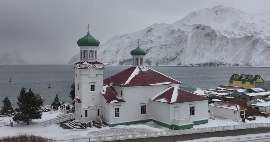 Aerial view of the serene russian orthodox church surrounded by snowy mountains and a tranquil sea, Unalaska, United States.